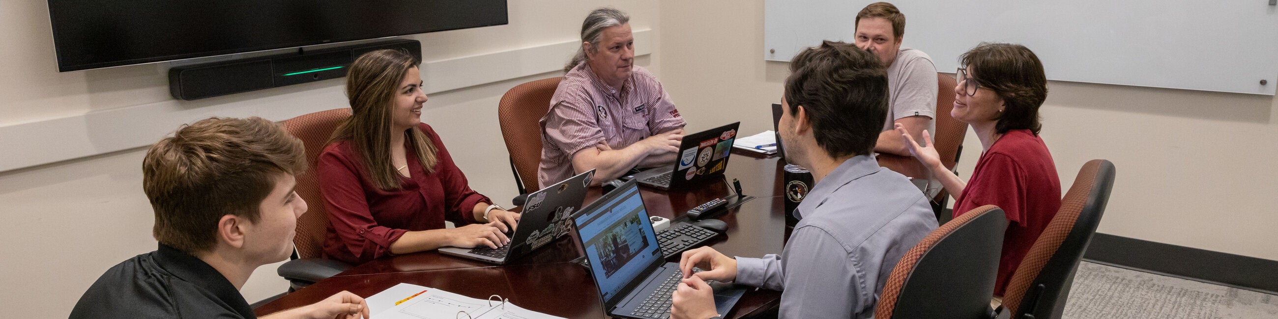 Six employees working together on their laptops in a conference room.
