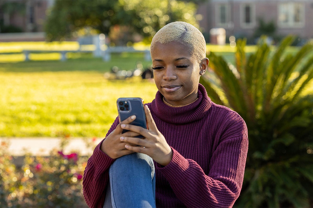 Female student sitting outside on her phone.